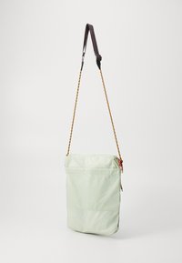 Világos zöld nylon válltáska, felső cipzáras zárással, állítható mintás pánttal és elülső zsebbel a plusz tárolás érdekében.