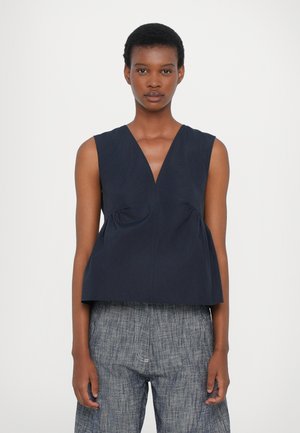 Navy sleeveless top with a deep V-neck, rounded hem, and soft, textured fabric. Features gathered detailing at the sides.