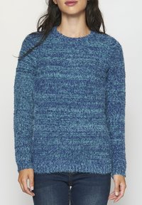 Pull en tricot bleu avec une apparence texturée et pelucheuse. Encolure et poignets côtelés. Le motif présente des nuances variées de bleu.