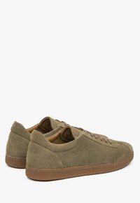 Zielono-oliwkowe zamszowe sneakersy o niskim kroju, okrągłym czubku i płaskiej brązowej gumowej podeszwie. Posiadają dopasowane sznurowadła i wyściełane wnętrze.