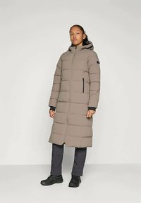 Casaco de puffer longo, bege, com fecho de correr à frente, capuz e bolsos laterais. Apresenta seções acolchoadas, punhos elásticos e uma textura suave.