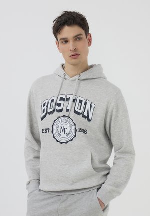 Felpa grigia con cappuccio regolabile e tasca frontale. Presenta la scritta "BOSTON" in grassetto blu navy e un logo grafico rotondo al centro. Tessuto morbido.