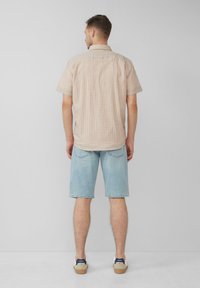 Korte mouwen overhemd met een ruitpatroon in oranje en blauw op een lichte achtergrond, gecombineerd met lichtblauwe denimshorts en sneakers.