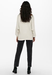 Pull en maille texturée légère de couleur écru, coupe ample, manches larges. Associé à un jean foncé taille haute et des bottines noires à talons blocs.