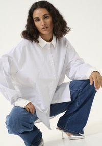 Langærmet hvid skjorte med lysegrå striber, knappet foran, og kontrastende hvid krave, parret med blå denim bukser og sølvhæle.