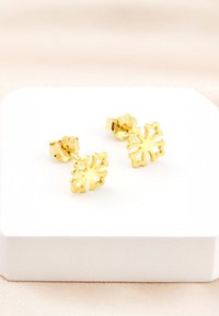 Orecchini a pendente placcati in oro con un design a fiocco di neve, caratterizzati da dettagli intagliati intricati e una finitura lucida, esposti in una scatola bianca.