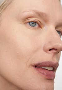 Närbild av ett ansikte med slät, ljus hy. Utmärkande drag inkluderar ljusblå ögon och naturlig läppfärg. Minimal makeup, mjukt ljus.