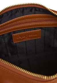 Notranjost rjave usnjene torbe z črno tkaninsko podlogo, ki ima ozke vertikalne črte. Vidni so zlat zadrga in oznaka "Pepe Jeans".