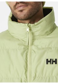 Světlá zelená bunda typu puffer s vysokým límcem, předním zipem a černým logem na levé straně. Hladká textura s prošívaným designem.
