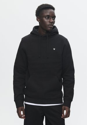 Black hooded sweatshirt made of textured fabric, featuring a front kangaroo pocket and subtle logo on the chest. Standard fit with drawstrings.
