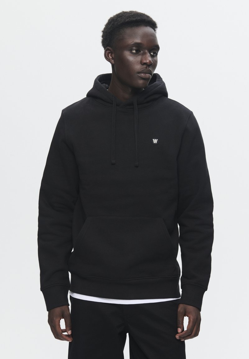 Black hooded sweatshirt made of textured fabric, featuring a front kangaroo pocket and subtle logo on the chest. Standard fit with drawstrings.