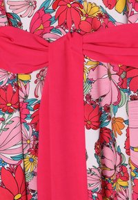 Vestido floral con un vibrante cinturón rosa. La tela muestra grandes flores multicolores en tonos de rosa, rojo, amarillo y verde.
