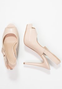 Scarpe coniugate nude con tacco alto e punta aperta, realizzate in pelle liscia. Presentano un elegante dettaglio a fiocco e un tacco a stiletto sottile.