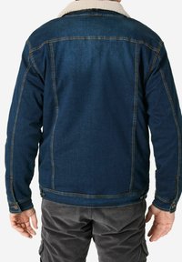 Denim jacket in dark blue with a shearling collar, visible stitching, and buttoned cuffs, paired with grey corduroy pants.