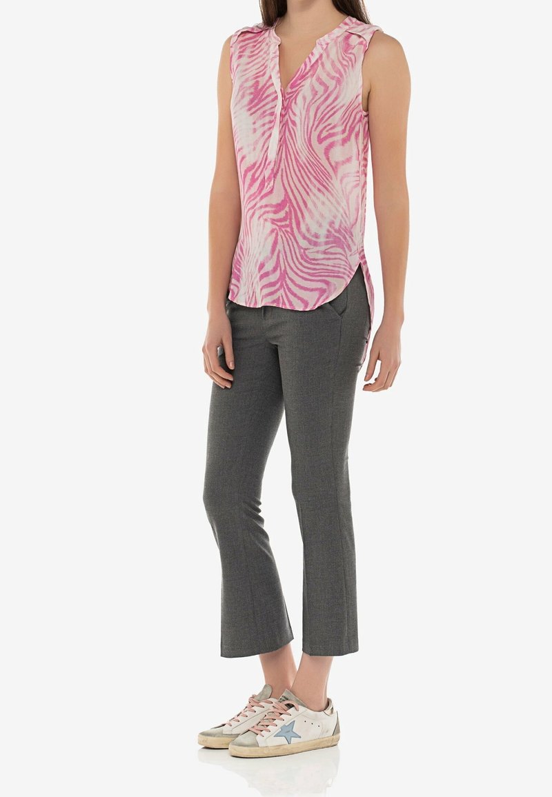 Femme portant un chemisier sans manches à motif rose et blanc, un pantalon gris court et des baskets blanches avec des touches d’étoile bleues.