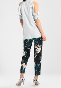 Camicia azzurro chiaro con spalle scoperte abbinata a pantaloni neri con fiori in rosa e verde, completata da scarpe col tacco argentate.