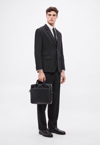 Czarna skórzana teczka z górnymi uchwytami, gładka faktura i minimalistyczny design. Noszona z czarnym garniturem i eleganckimi butami.