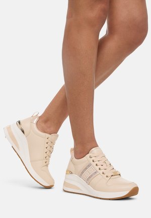Beige sneakers with a glossy finish, featuring gold accents, patterned side stripe, and a thick white wedge sole. Laces are in a classic style.