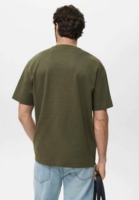 Olive green oversized t-shirt made of cotton, short sleeves, crew neck, and a straight hem, paired with light blue jeans.