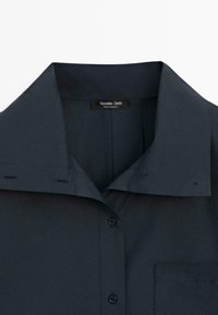 Ciemnogranatowa koszula na guziki z kołnierzykiem, z kieszenią na piersi, widocznym przeszyciem i metką Massimo Dutti wewnątrz kołnierza.
