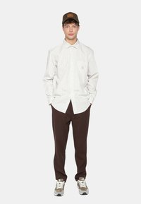 Chemise à manches longues rayée en blanc et gris clair, associée à un pantalon marron. Casquette marron et baskets grises avec des accents blancs. Design simple.