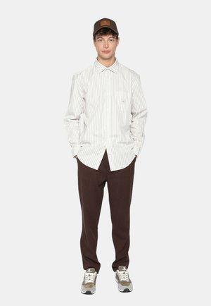 Chemise à manches longues rayée en blanc et gris clair, associée à un pantalon marron. Casquette marron et baskets grises avec des accents blancs. Design simple.