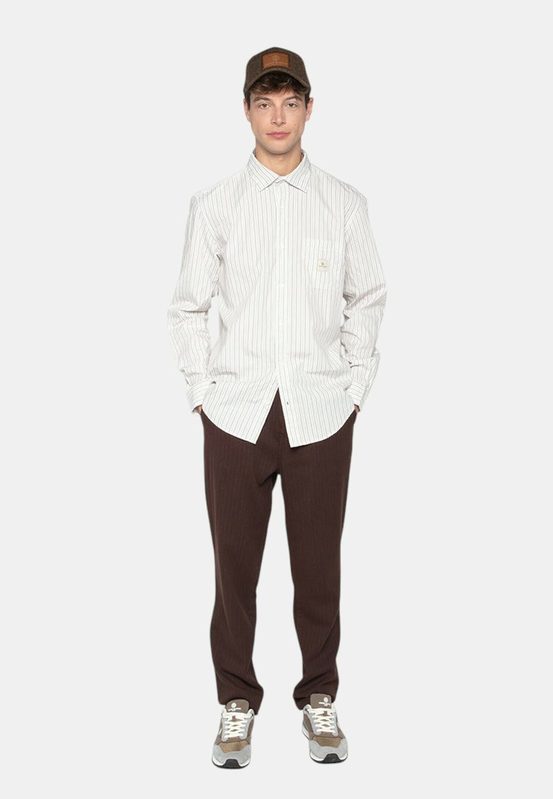 Chemise à manches longues rayée en blanc et gris clair, associée à un pantalon marron. Casquette marron et baskets grises avec des accents blancs. Design simple.