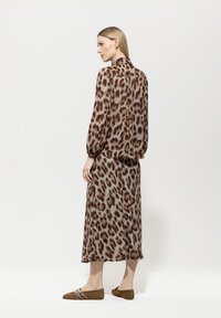 Hemdbluse mit Leopardenmuster, lockerer Passform, langen Ärmeln und Kragen, kombiniert mit einem passenden Midirock im Leopardenmuster und braunen Slippers.