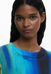 Knit sweater in blue and green gradient, featuring a round neckline and smooth texture. No distinct patterns or hardware visible.