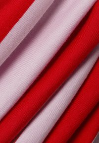 Stacked fabrics in varying shades of red and pink, featuring smooth, knitted textures and horizontal stripes on some pieces.