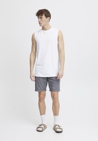Hvit ermeløs skjorte, grå shorts med rullet kant, hvite sokker og brune sandaler. Enkelt design, lett materiale.