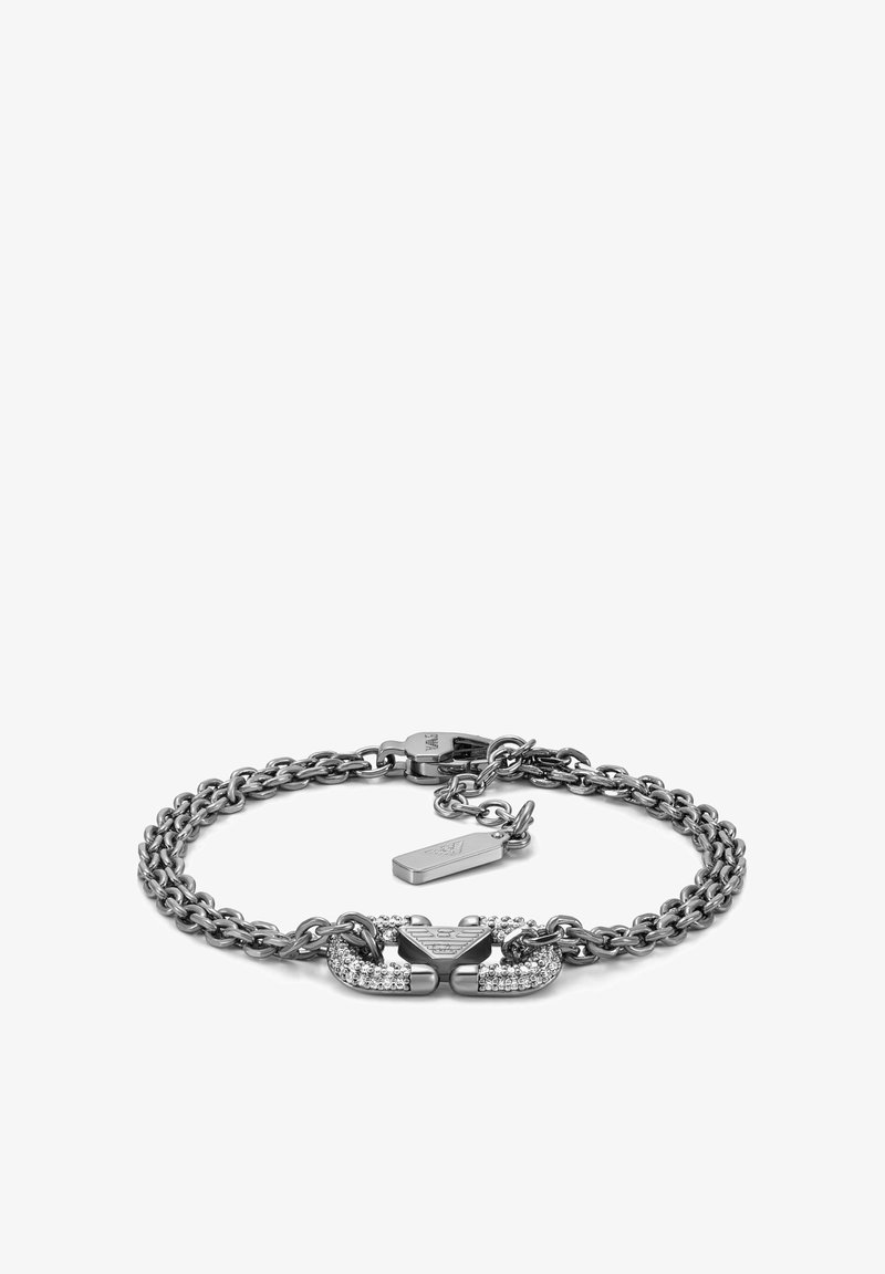 Bracelet chaîne en argent avec double fermoir incrusté de petits cristaux et une petite étiquette rectangulaire de marque près du fermoir.