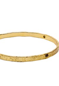 Złota bransoletka w formie bangla z teksturowaną powierzchnią, z młotkowanym wykończeniem i dwoma małymi ciemnymi kamieniami osadzonymi w projekcie.
