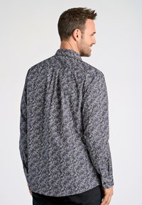 Långärmad skjorta i mörkblått med blommönster. Har en knapp-ner krage och en rak rygg med axelkil, tillverkad av lättviktig tyg.