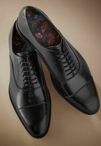 Zapatos de vestir de cuero negro con diseño de puntera, con un acabado suave y cordones de seis ojales. Forro con estampado floral visible en el interior.