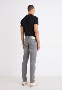 Jeans de mezclilla gris con detalles de costura y bolsillos traseros, llevados con una camiseta negra y zapatillas blancas, vistos desde atrás.