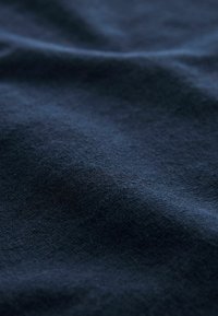 Tessuto blu navy, texture morbida, superficie leggermente stropicciata e colore uniforme. Nessun motivo visibile o dettagli hardware.