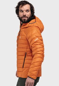 Orangene Steppjacke mit gepolstertem Design, Kapuze, schwarzen Reißverschlüssen und einem Logo am Ärmel. Glatte Textur mit schlanker Silhouette.