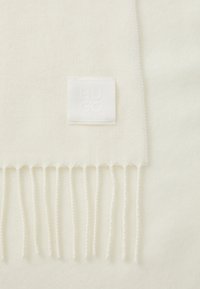 Écharpe blanche avec un motif à chevrons, dotée d'une étiquette texturée "HUGO" et de franges le long d'un bord.