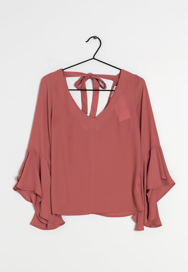 Blouse rose avec manches longues évasées et décolleté en V profond. Dos avec fermeture à nouer et deux lanières. Tissu lisse et léger.