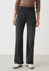Zwart high-waisted jeans met een relaxte rechte pasvorm, voorzien van subtiele stiksels en voorzakken, gecombineerd met witte sneakers.