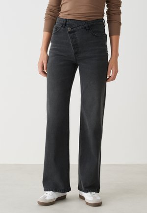 Hochtaillierte schwarze Jeans mit einem lässigen geraden Schnitt, ausgestattet mit dezenten Nähten und Fronttaschen, kombiniert mit weißen Sneakern.