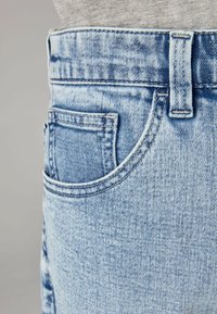 Jasnoniebieskie dżinsy z wysokim stanem, kieszenią z przodu oraz zaczernioną strukturą z widocznymi detalami szwów.
