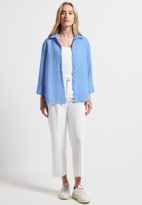 Camicia button-up in lino azzurro chiaro, pantaloni bianchi a gamba larga e sneaker color crema. Fit casual, design con colletto e silhouette rilassata.