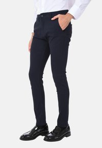 Pantaloni slim-fit blu navy realizzati in una fusione di cotone testurizzato, dotati di tasche laterali e chiusura a bottone, abbinati a mocassini neri lucidi.