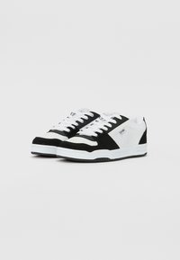 Black and white sneakers with suede and leather materials. Features perforated sides, white laces, and a rubber sole. Classic sporty design.
