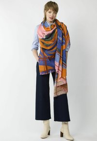 Mehrfarbiger Schal aus weichem Material mit Mustern in Orange, Blau, Grün und Pink, mit fransigem Rand, über die Schultern drapiert.