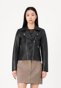 Svart skinnskinnjakke med glidelåslommer, spiss krage og asymmetrisk frontglidelås. Jevn tekstur, tettsittende design.