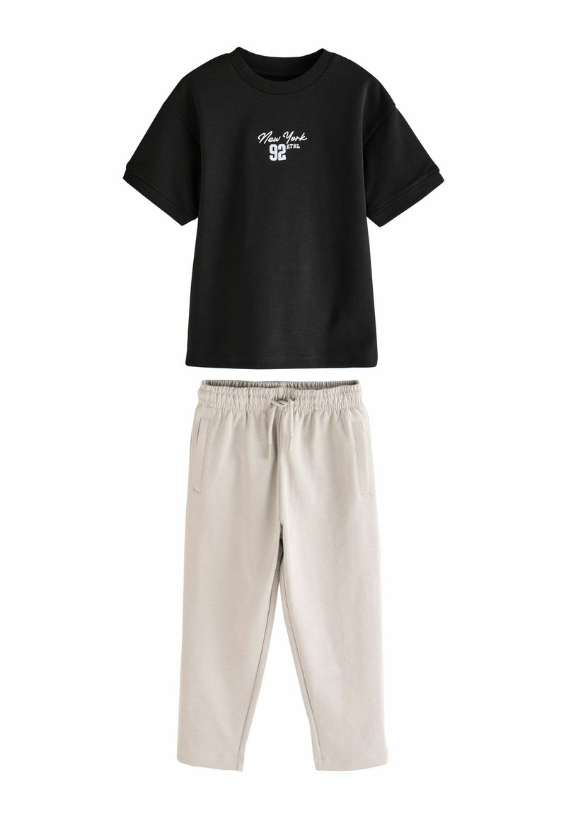 Sort kortærmet t-shirt med hvid "New York 92" tekst; parret med lysebeige joggerbukser med sidelommer og elastisk talje.