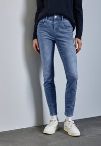 Ljusblå skinny jeans i denim, med en klassisk femfickedesign och metallknappstängning, kombinerade med vita sneakers.